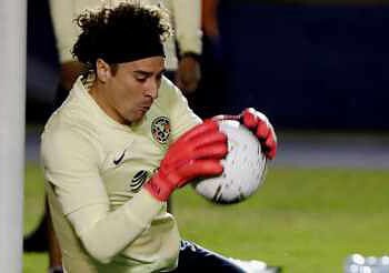 Portero de fútbol entrenando con balón en el arco, en una cancha profesional.