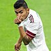 Jugador de fútbol en acción en el campo con uniforme blanco y tatuajes visibles.
