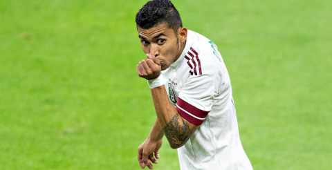 Jugador de fútbol en acción en el campo con uniforme blanco y tatuajes visibles.
