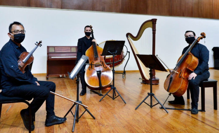 Músicos tocando con instrumentos de cuerda en concierto en sala de ensayo.