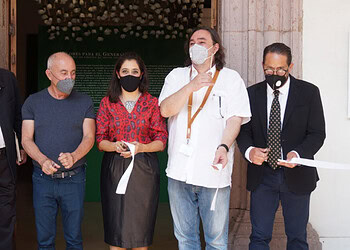 Diversos profesionales en evento de apertura con mascarillas y documentos, en un entorno formal y cultural.