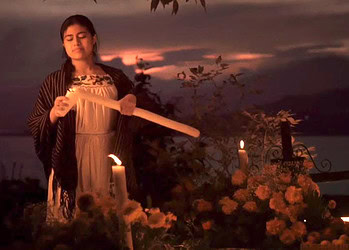 Veladora encendida en día de víacrucis con mujer rezando en noche oscura al atardecer en México.
