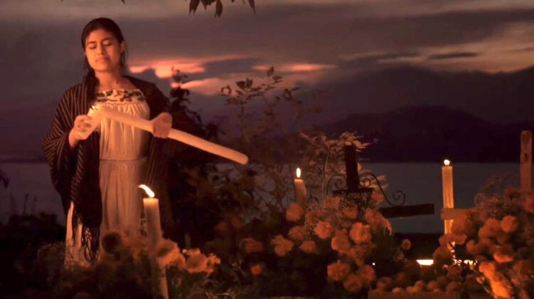 Veladora encendida en día de víacrucis con mujer rezando en noche oscura al atardecer en México.