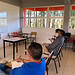 Estudiante presentando en aula con otros alumnos, aula moderna con vista a la naturaleza, ambiente de aprendizaje tranquilo y innovador.