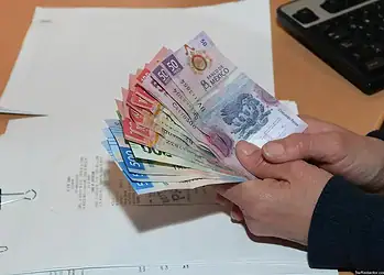 Dinero en efectivo de diferentes denominaciones en manos humanas en oficina moderna.