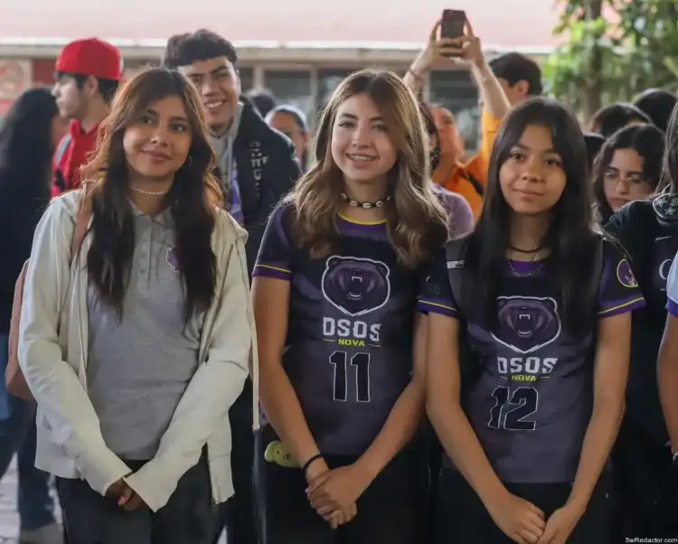 Chicas jóvenes en uniforme deportivo en evento escolar con otros estudiantes en el fondo.