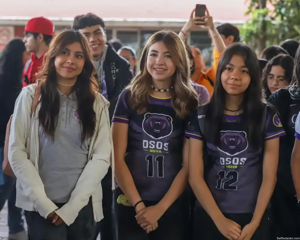 Chicas jóvenes en uniforme deportivo en evento escolar con otros estudiantes en el fondo.
