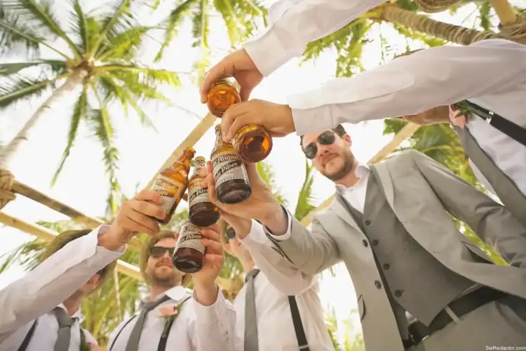 Barras de bebidas en una reunión tropical con personas sonriendo y brindando bajo palmeras.