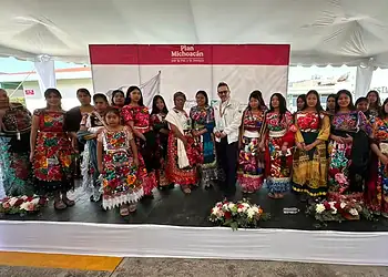 Vestido tradicional mexicano en un evento cultural con grupo de personas en un escenario.