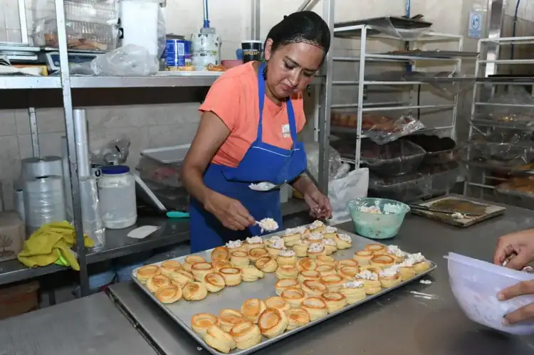 Mujer preparando y decorando pasteles en una cocina industrial.