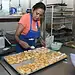 Mujer preparando y decorando pasteles en una cocina industrial.