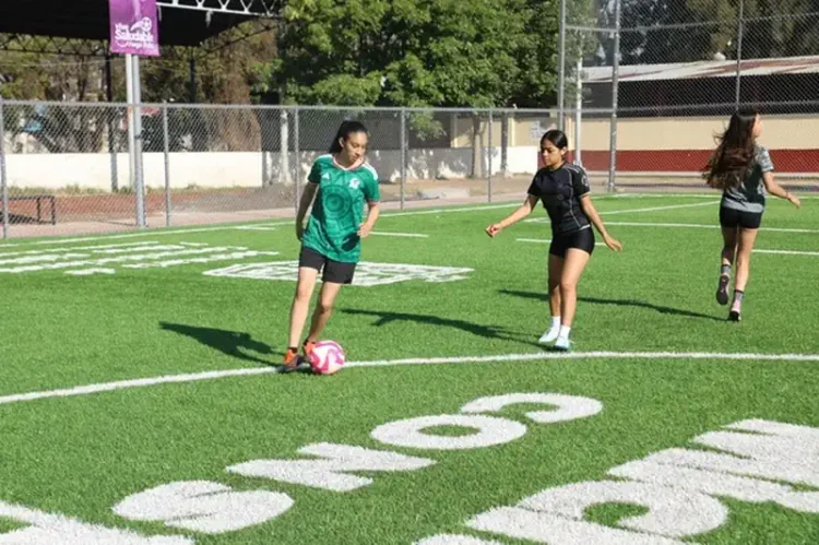 Balón de fútbol y niñas jugando en campo de césped artificial.