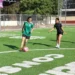 Balón de fútbol y niñas jugando en campo de césped artificial.