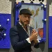 El hombre en la galería de arte con fondo azul y obras decorativas.