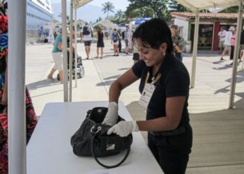 Persona revisando una maleta en un puesto de control en un evento al aire libre.
