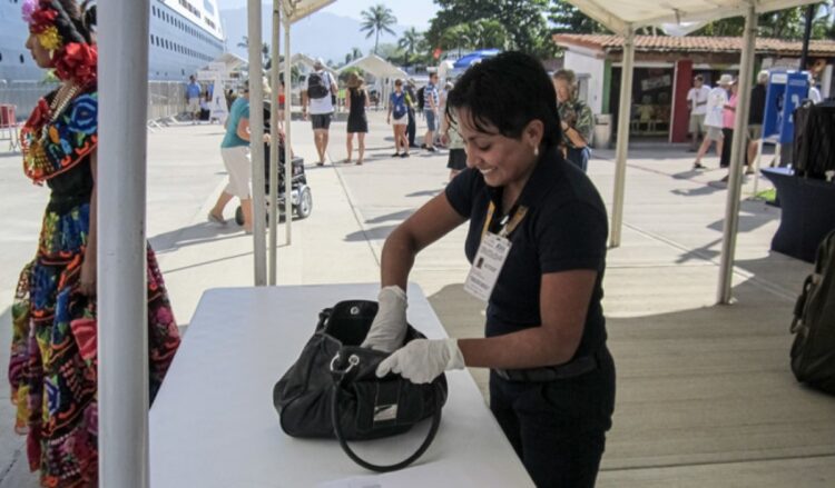 Persona revisando una maleta en un puesto de control en un evento al aire libre.