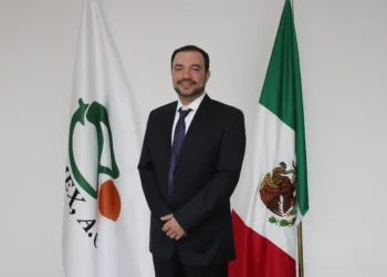 José Ángel Crespo, de pie frente a banderas de México y organización agrícola, en un entorno institucional.