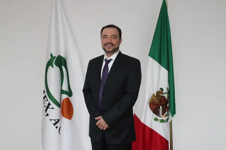José Ángel Crespo, de pie frente a banderas de México y organización agrícola, en un entorno institucional.