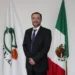 José Ángel Crespo, de pie frente a banderas de México y organización agrícola, en un entorno institucional.