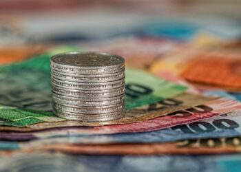 Montón de monedas sobre billetes de diferentes denominaciones en colores variados.