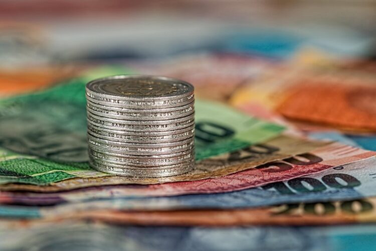 Montón de monedas sobre billetes de diferentes denominaciones en colores variados.
