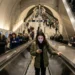 Amplia afluencia de pasajeros en estación de metro con personas usando teléfonos y subiendo escaleras mecánicas.