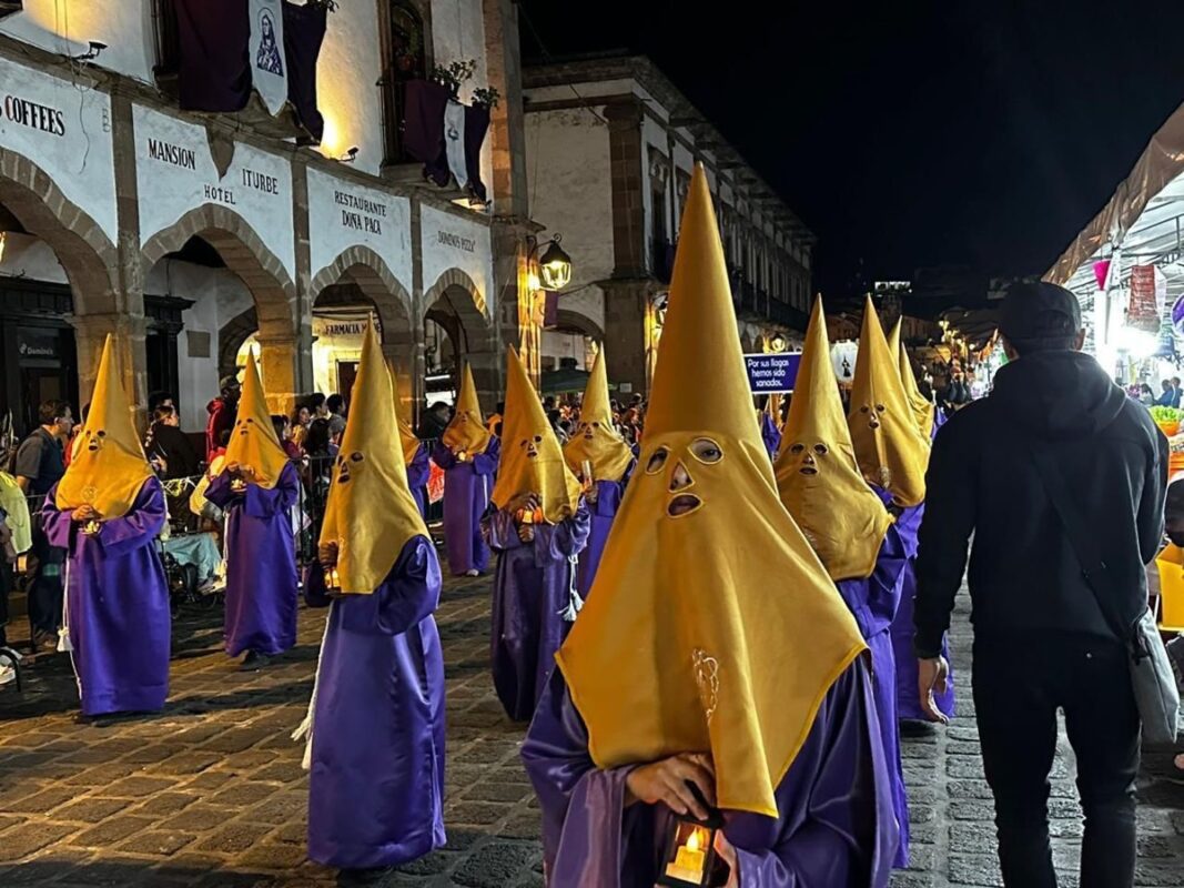 Disfraces de Semana Santa con capuchas amarillas y túnicas moradas en una calle histórica.