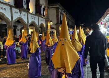 Disfraces de Semana Santa con capuchas amarillas y túnicas moradas en una calle histórica.
