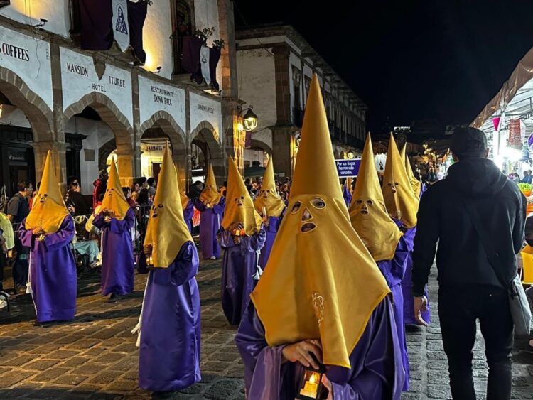 Disfraces de Semana Santa con capuchas amarillas y túnicas moradas en una calle histórica.