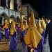 Disfraces de Semana Santa con capuchas amarillas y túnicas moradas en una calle histórica.