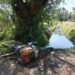Bomba de agua robada junto a un canal con árboles y vegetación, evidencia de huachicol de agua en área rural.