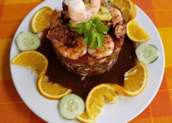 Plato de mariscos con camarones, pulpo y limón, decorado con cilantro y acompañado de rodajas de pepino y naranja en un plato.