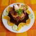 Plato de mariscos con camarones, pulpo y limón, decorado con cilantro y acompañado de rodajas de pepino y naranja en un plato.