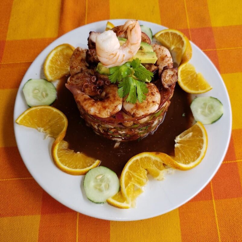 Plato de mariscos con camarones, pulpo y limón, decorado con cilantro y acompañado de rodajas de pepino y naranja en un plato.