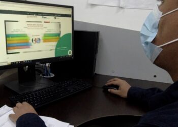 Persona usando computadora con pantalla de plataforma digital de certificación cárnica en oficina.