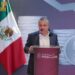 Auto en Michoacán, con bandera mexicana y fondo de monedas y símbolo de dinero, en una conferencia de prensa.