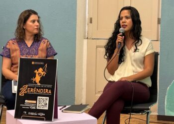 Mujer hablando en evento cultural con micrófono en mano.