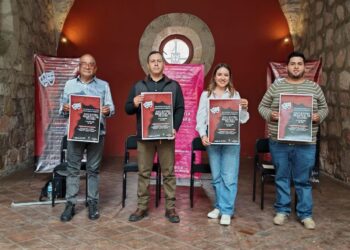 Cartel de evento teatral en un espacio histórico con cuatro personas sosteniendo carteles.