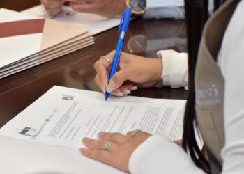 Persona firmando documento en mesa de trabajo.