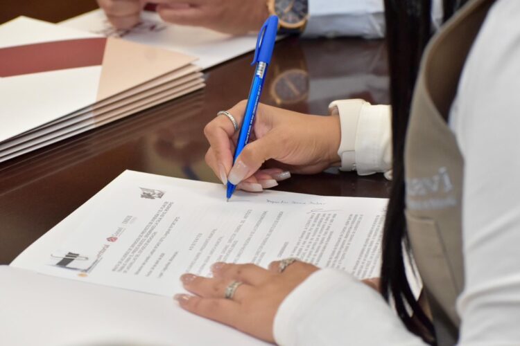 Persona firmando documento en mesa de trabajo.