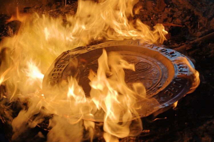Manhole cover burning amidst flames, symbolizing cultural resilience and social issues in Michoacán.