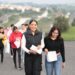 Estudiantes con documentos en mano caminando en un camino rural con paisaje de colinas y vegetación, en un día soleado.