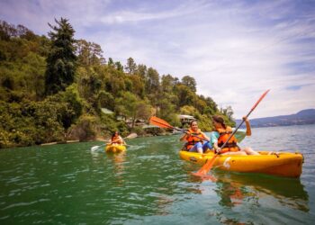 Personas remando en kayak en el lago Zirahuén, rodeados de naturaleza y montañas, disfrutando del turismo deportivo en Michoa.