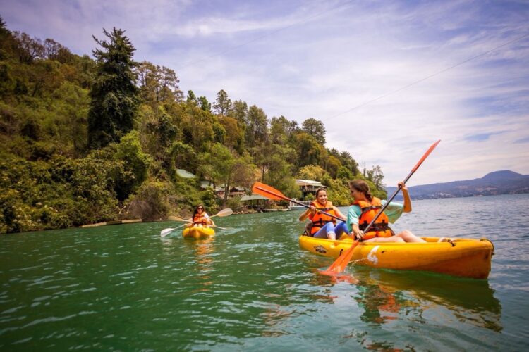 Personas remando en kayak en el lago Zirahuén, rodeados de naturaleza y montañas, disfrutando del turismo deportivo en Michoa.