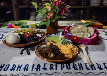 Colorido plato tradicional con diversos ingredientes y sabores en una mesa decorada con flores y textiles típicos.