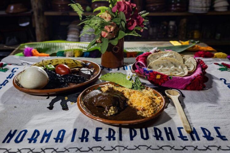 Colorido plato tradicional con diversos ingredientes y sabores en una mesa decorada con flores y textiles típicos.