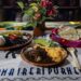 Colorido plato tradicional con diversos ingredientes y sabores en una mesa decorada con flores y textiles típicos.