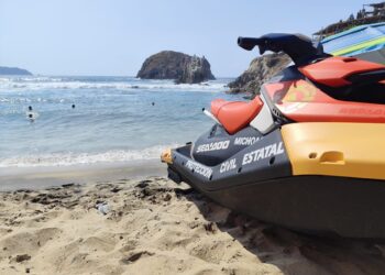 Moto acuática en playa con olas y rocas en el fondo, personal de rescate en acción en Michoacán.