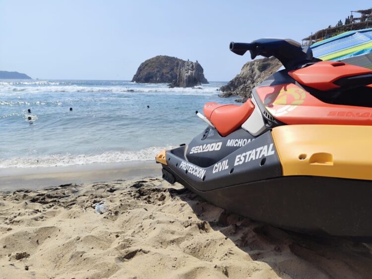 Moto acuática en playa con olas y rocas en el fondo, personal de rescate en acción en Michoacán.
