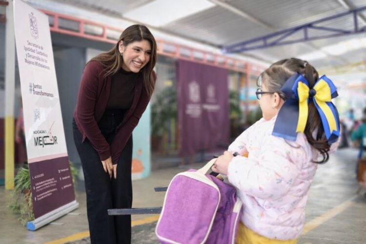 Mujer sonriente conversa con niña en evento de inscripción para programa "Las Niñas Pueden".